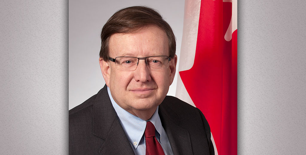 The Honourable Percy Downe A portrait of an older man in front of a Canadian flag