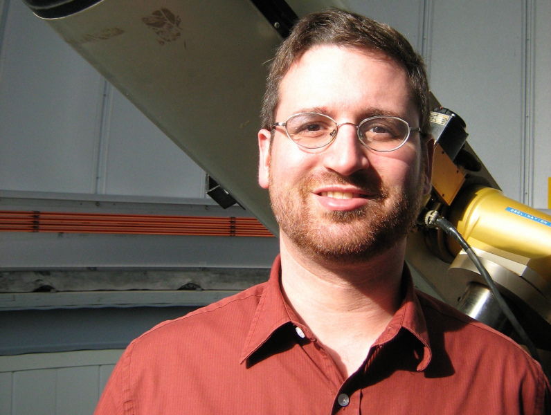 Dr. Gregory Sivakoff A smiling man in front of a telescope