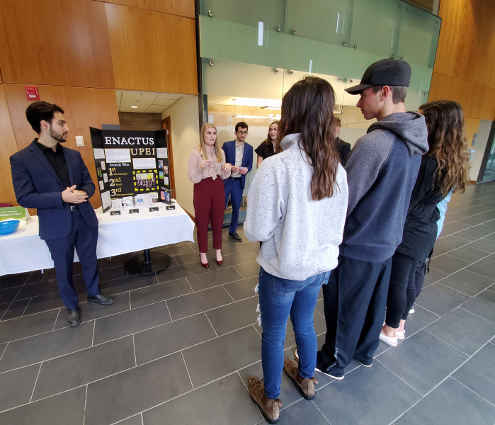 Enactus UPEI members Dan Timen and Ashley Doucette speak with a group of students at the UPEI Open House in September 2019. A male and female student speak with a group of students