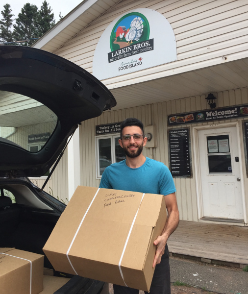 Co-op student Hani Mayaleh at Larkin Bros. Poultry with fresh supplies for the UPEI Food Bank A smiling male student loads a large box into the back of a vehicle