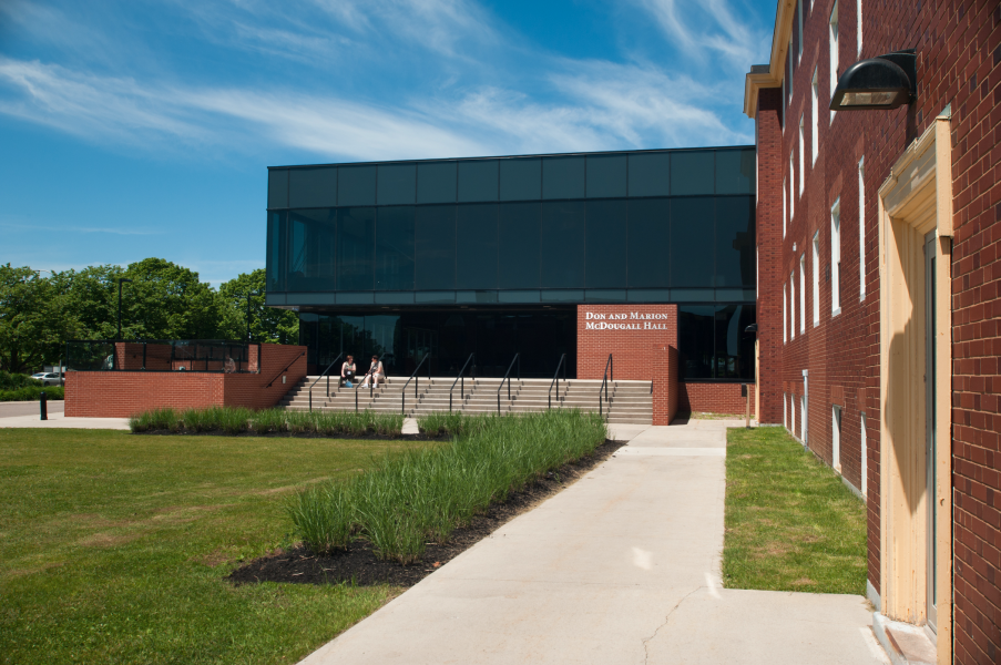 Don and Marion McDougal Hall A building of brick and dark glass with green grass in the foreground and a blue sky behind
