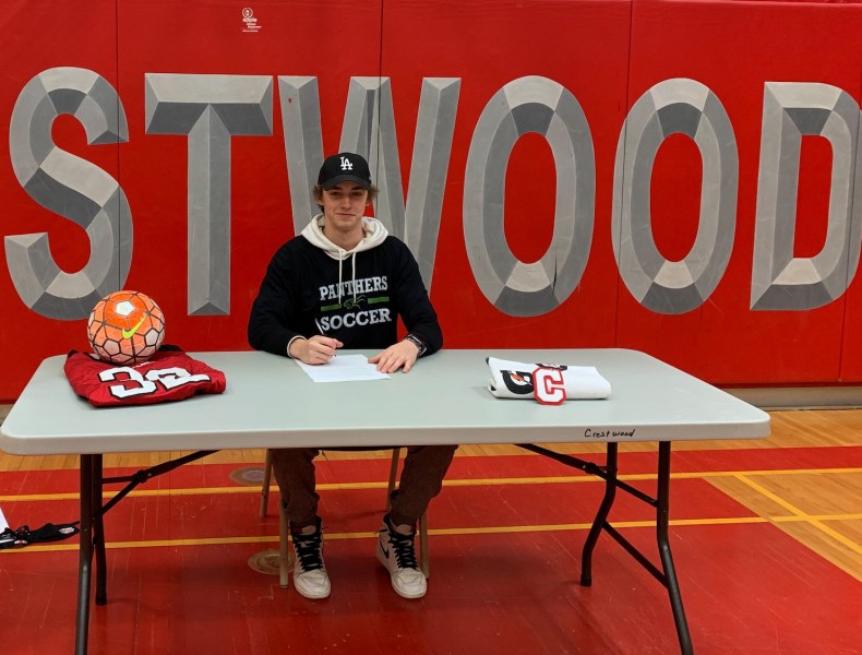 Scott Davis A smiling teenaged male sits at a table with the large logo fo CRESTWOOD secondary school behind him