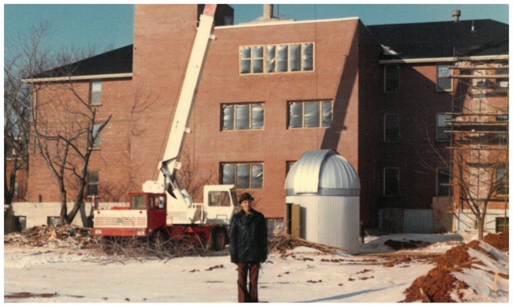 Professor Wonnacott stands next to the observatory before its installation in January, 1980 An aged photograph of a man standing next to a silver dome on the ground next to a brick building
