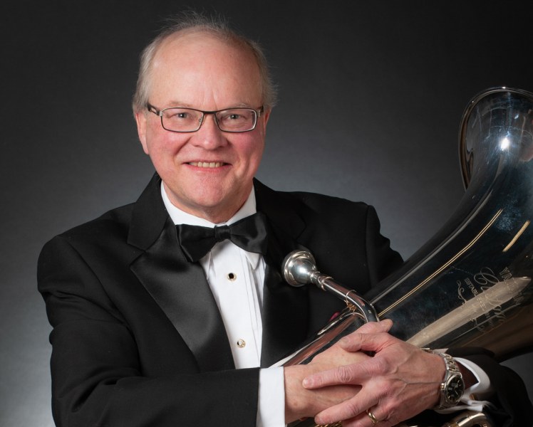 Dr. Greg Irvine A smiling man in a black tuxedo cradles a tuba in his arms