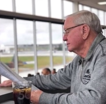 Billy Mulligan was not only passionate about the UPEI Panthers, but also was a big harness racing fan as seen here at Red Shores Racetrack Image of Billy Mulligan seated at a table with a beverage reading a harness racing program