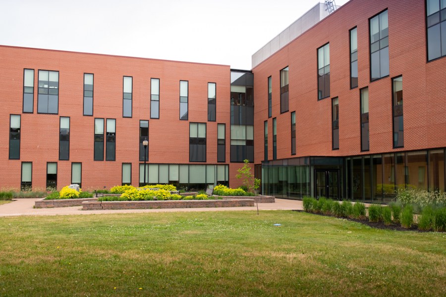 UPEI's Health Sciences Building A modern-looking red brick building, three stories with two prominent wings. A landscaped garden with sitting space on benches in the foreground.