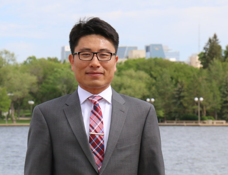 Dr. Xander Wang A professional-looking man n a grey suit stands in front of a river with trees and buildings on the opposite shore