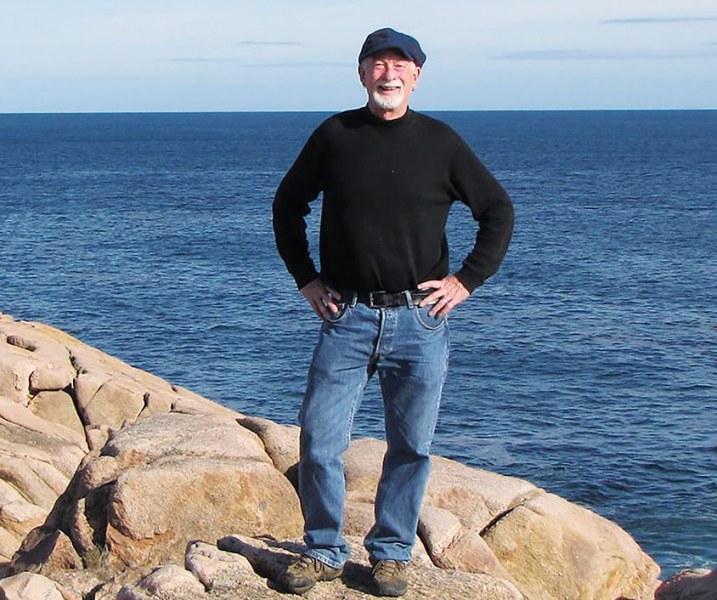 Dr. Richard Lemm An older man in jeans and a long black t-shirt stands on the rocks beside the sea