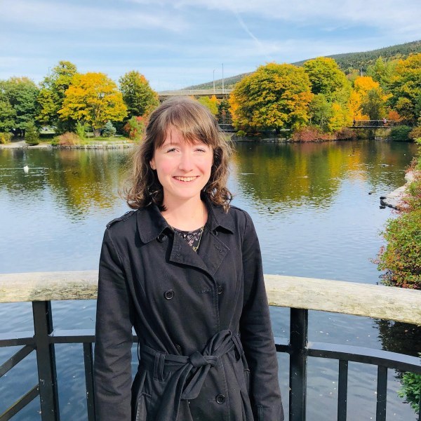Olivia Robinson A smiling young woman stands in front of a beautiful scene with a lake and trees