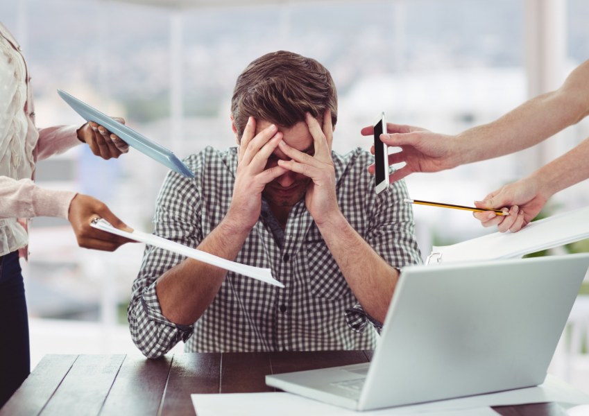 Background photo created by creativeart - www.freepik.com Man sitting at desk holding his head in his hands surrounded by stressors