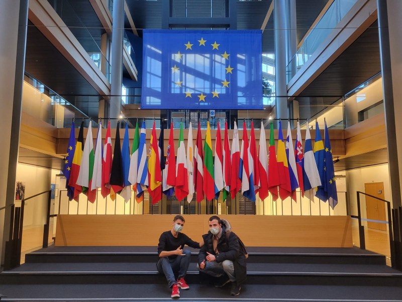 MGA students Nick Sablan from California (left) and Ignacio Martín from Madrid (right) visit the headquarters for the Council of Europe in Strasbourg, France Image of two men sitting on steps in front of a group of flags