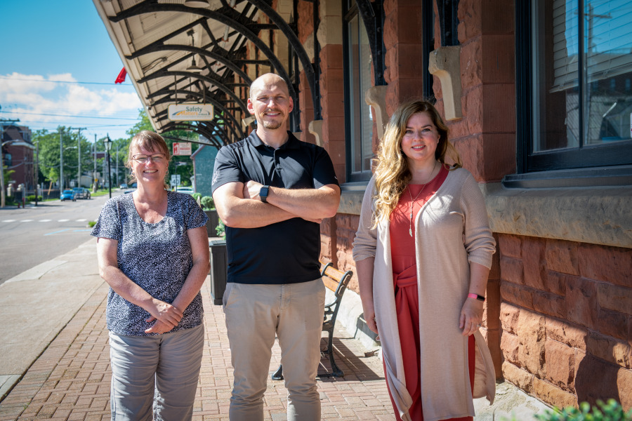 Standing in front of the former Charlottetown railway station are Barbara Rousseau, Applied Communications, Leadership, and Culture student; Dr. Josh MacFadyen, Canada Research Chair in Geospatial Humanities at UPEI; and Natalie Munn, heritage researcher and collections coordinator for the City of Charlottetown. The building, which now houses the Workers’ Compensation Board, is one of 80 sites included in a recently launched interactive digital story map of historical transportation in Charlottetown. Barbara Rousseau, Dr. Josh MacFadyen, and Natalie Munn stand next to the former Charlottetown Railway station.