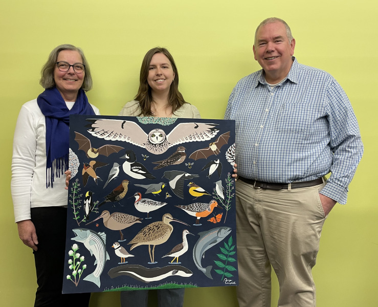 UPEI student Paige Campbell (centre) displays a painting of species at risk on PEI that she created to mark Earth Day as part of her Environmental Studies 4010 Public Scholars on Environmental Issues capstone course. Looking on are Dr. Carolyn Peach Brown, professor and director of the Environmental Studies program at UPEI, and University Librarian Donald Moses. Three people display painting.